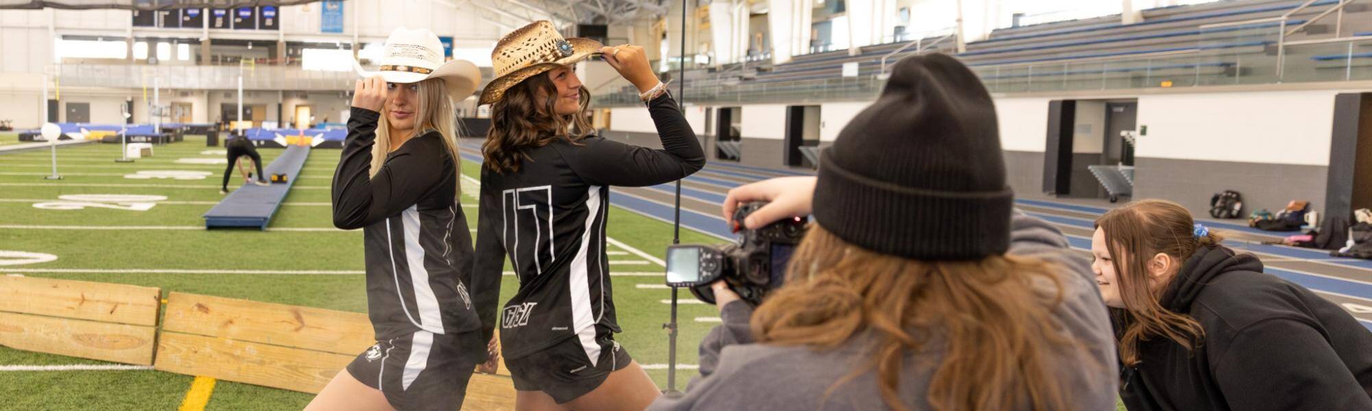 A photographer taking a photo of two lacrosse players wearing cowboy hats and cowboy boots